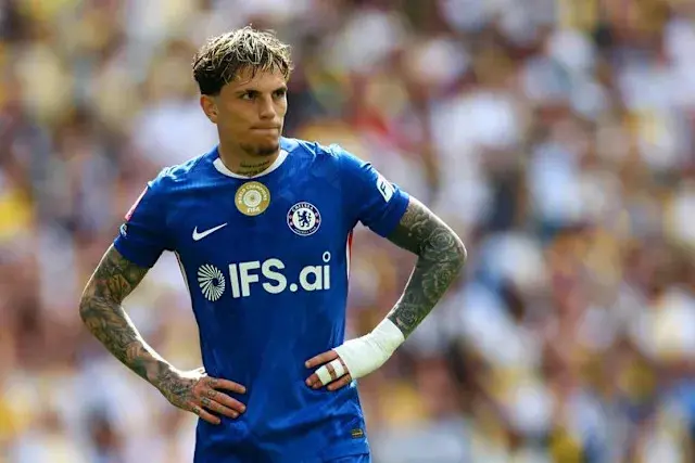 A football player in blue Chelsea kit looks on with a focused expression.