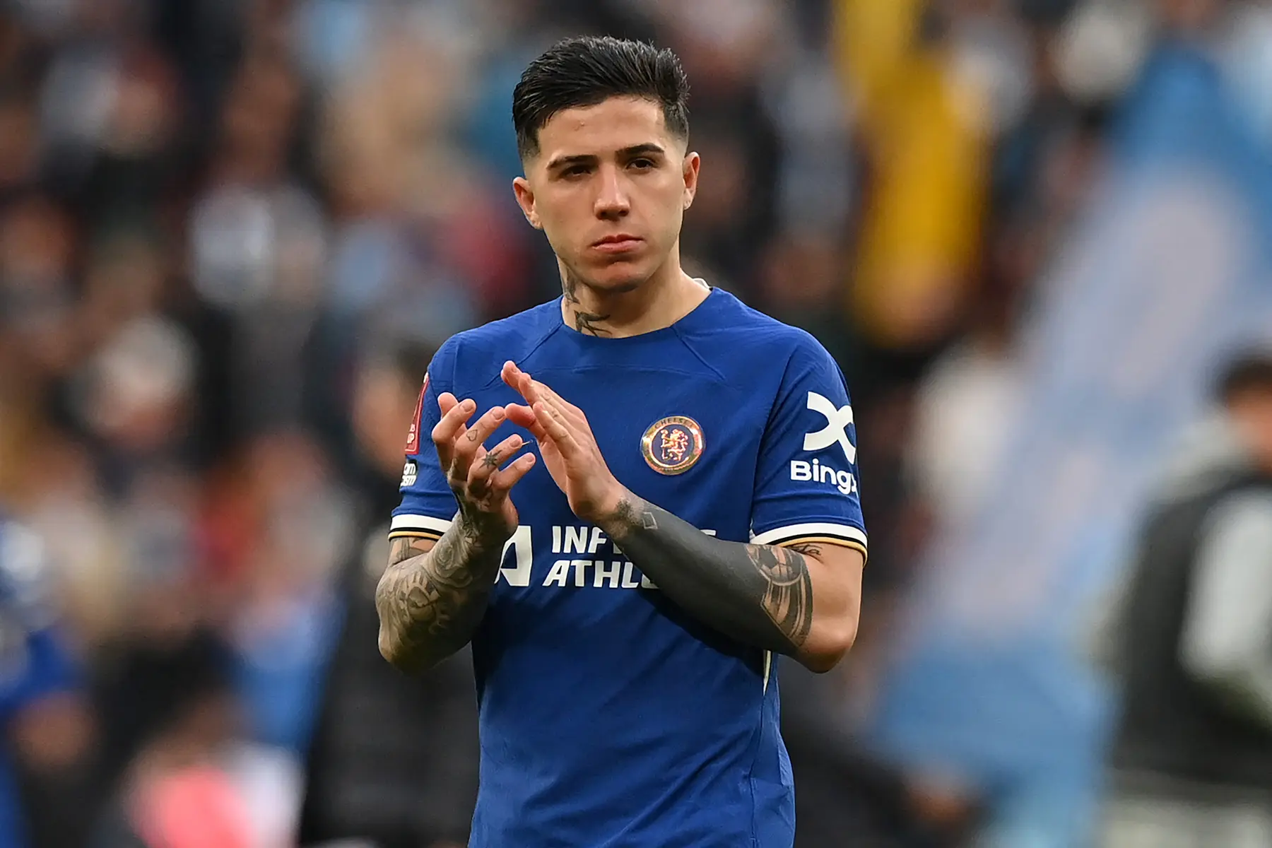 Enzo Fernandez in a blue Chelsea FC jersey, applauding fans after a match.