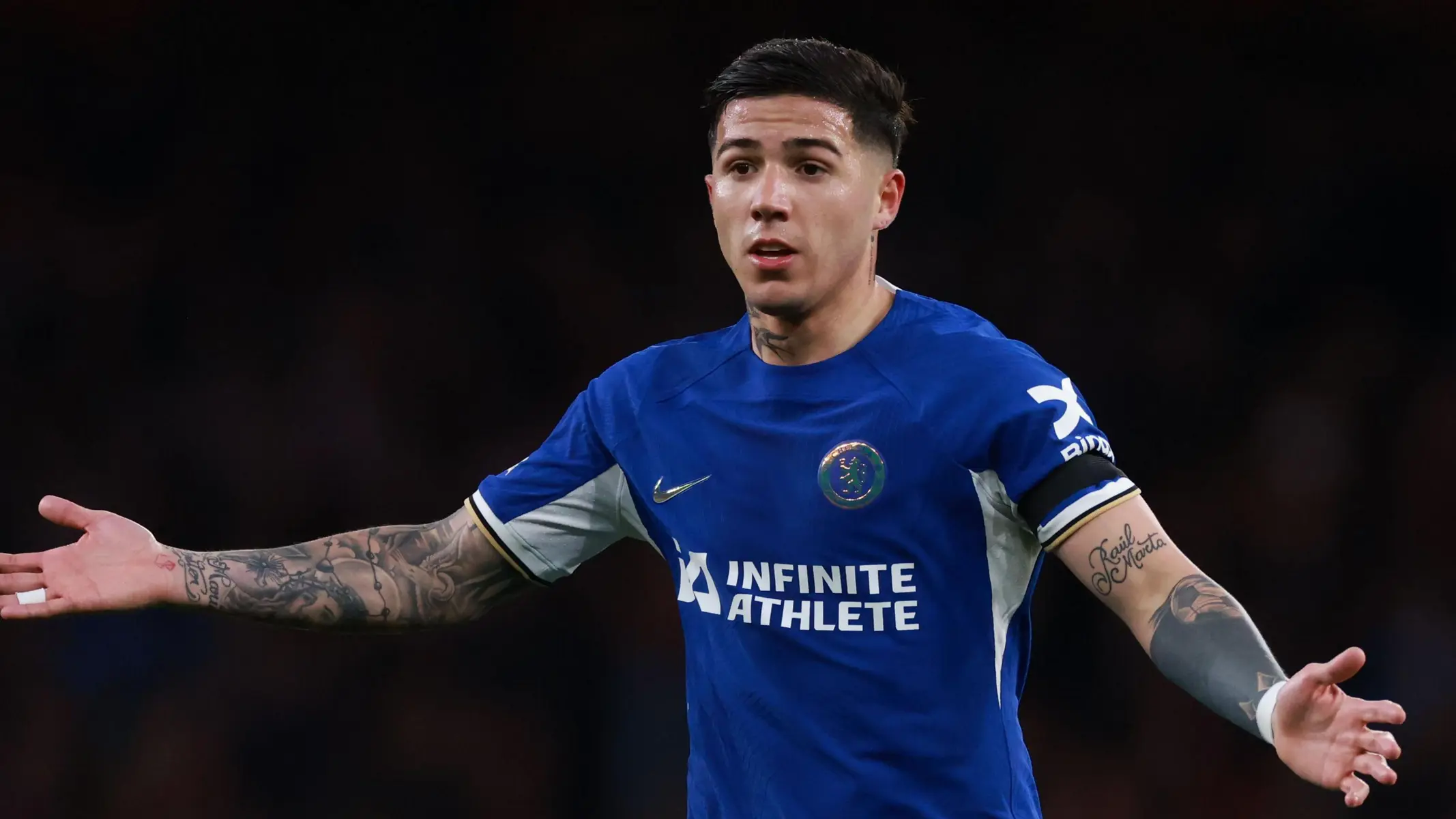 Enzo Fernandez in a blue Chelsea FC kit with arms outstretched on the pitch