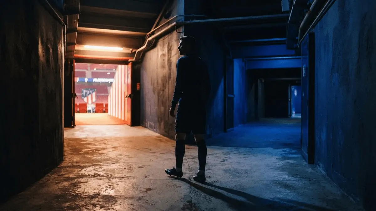 Footballer silhouette choosing between Atletico Madrid and Chelsea paths in dramatic stadium tunnel lighting