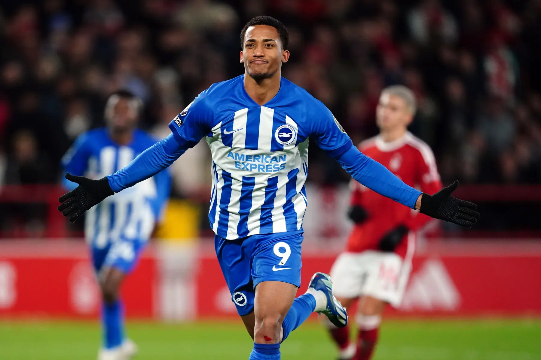 Brighton player celebrating a goal in a blue and white striped jersey.