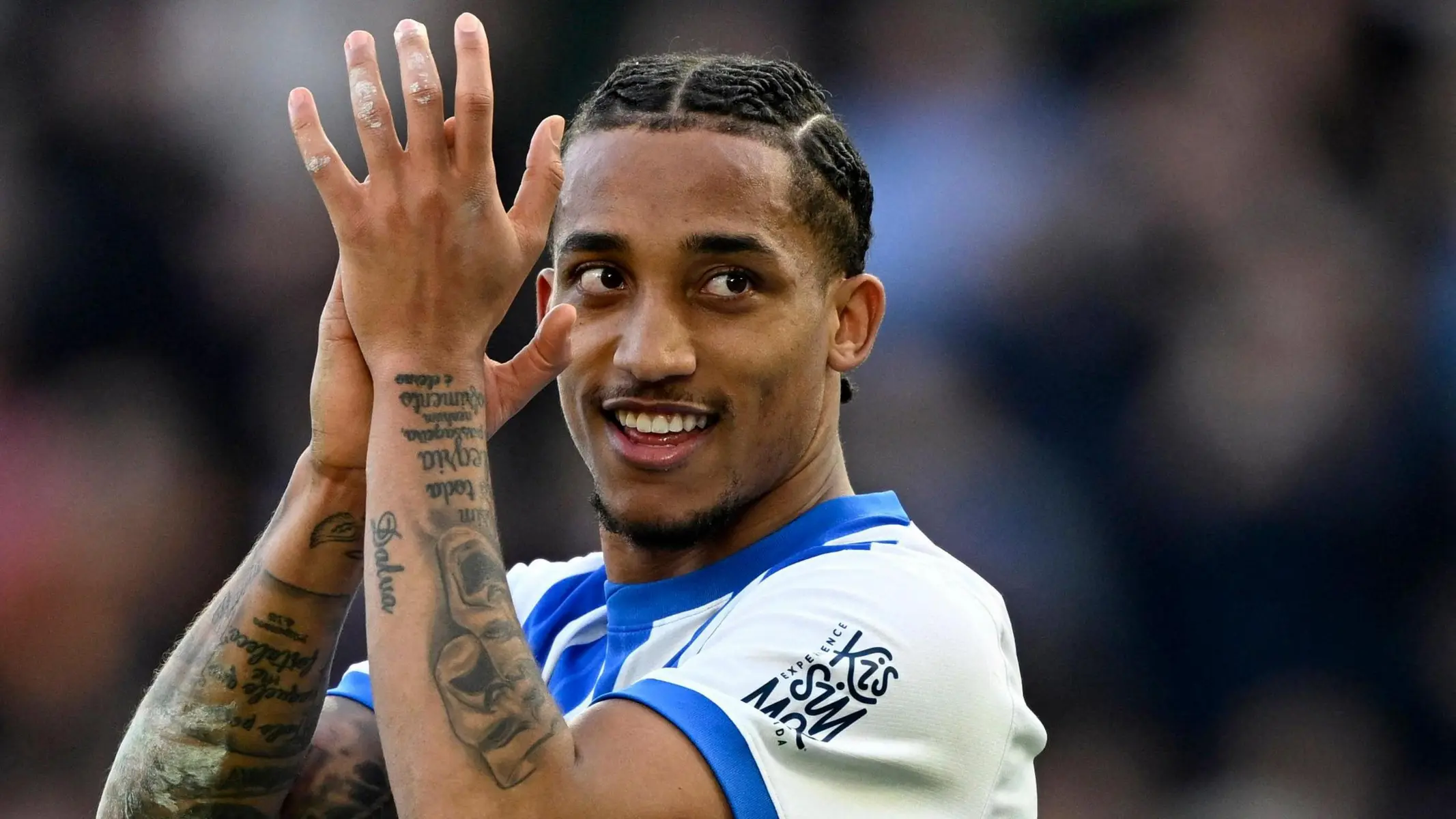 Brighton striker Joao Pedro clapping with a smile, showing tattoos on his arms and hands.