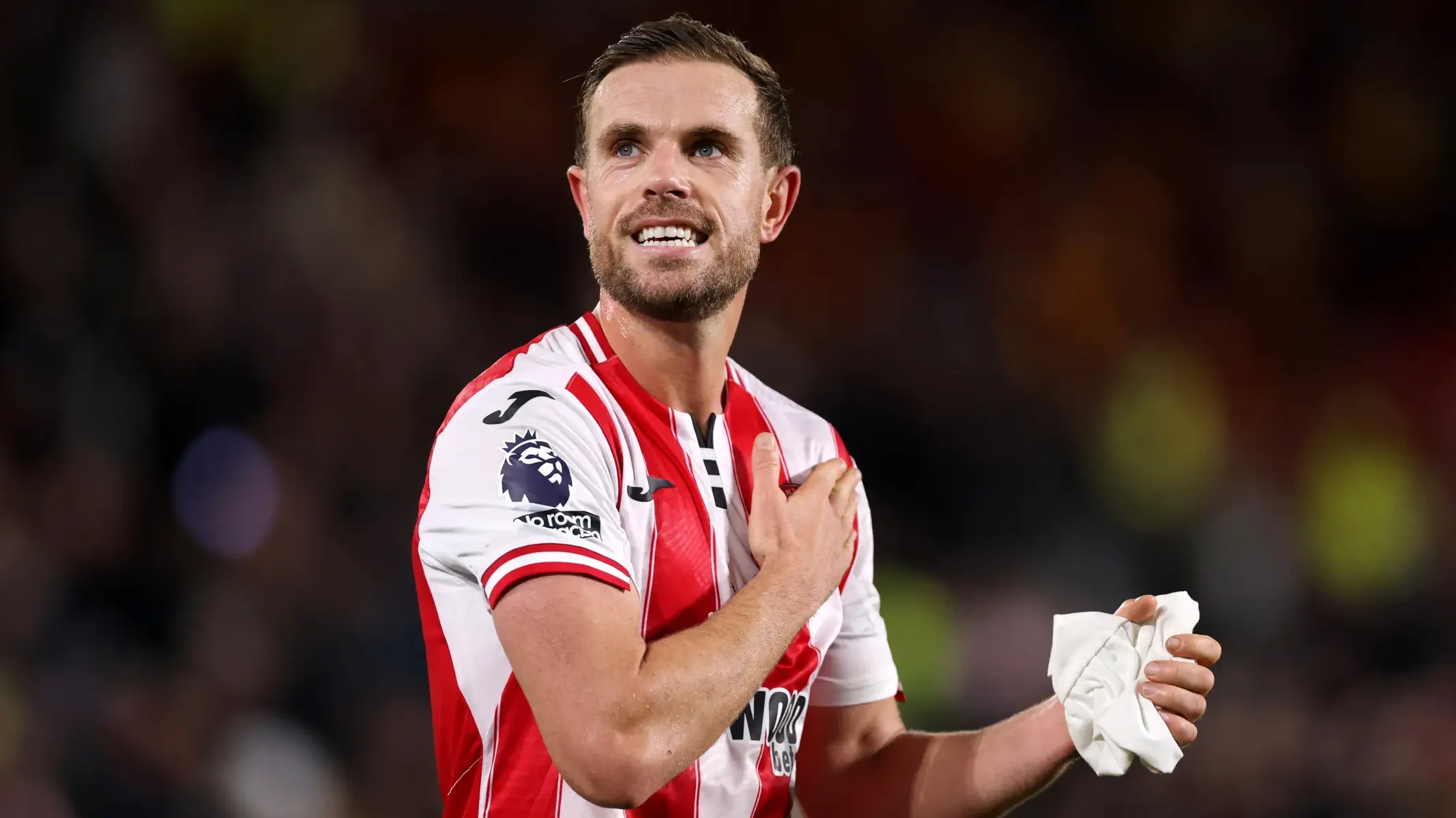 Jordan Henderson in a red and white striped Brentford FC jersey looking upwards