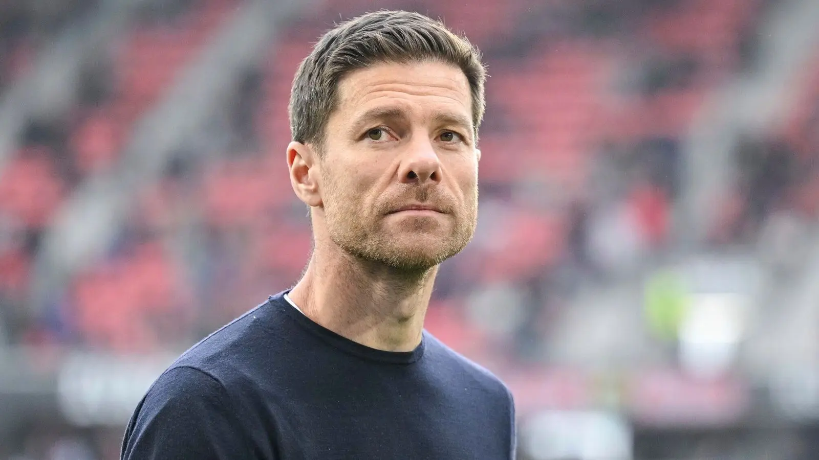 Close-up portrait of football manager Xabi Alonso looking off-camera at a stadium