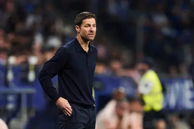 Xabi Alonso standing pitchside in a navy blue long-sleeve polo shirt during a football match