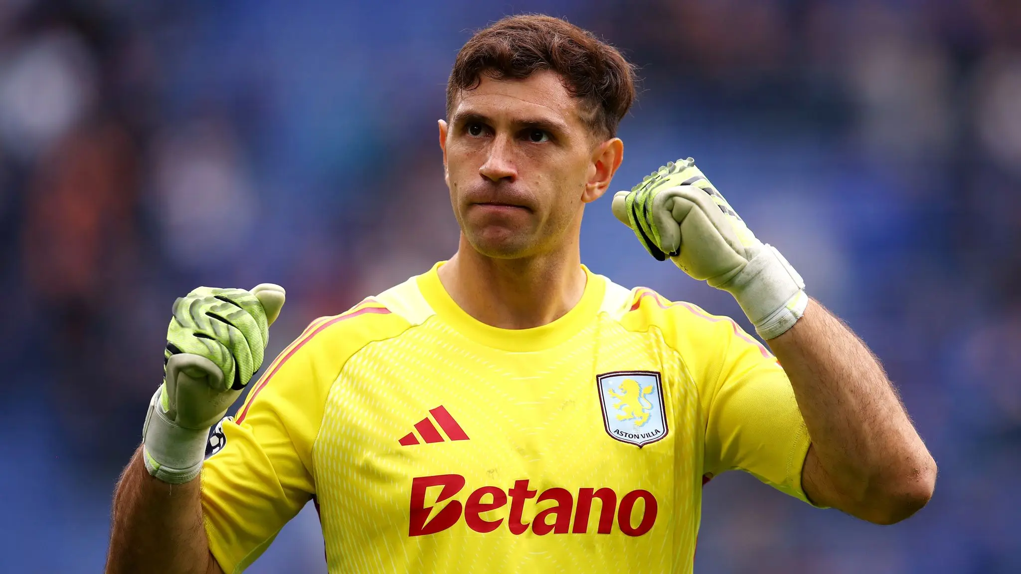 Aston Villa goalkeeper Emiliano Martinez wearing a yellow jersey and gloves, celebrating on the field.