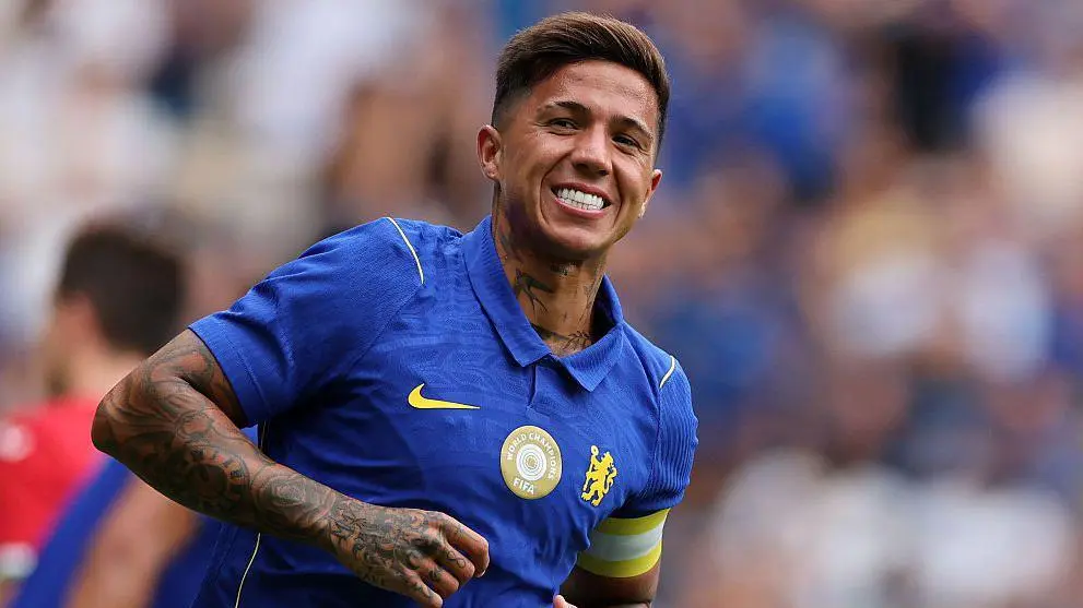 Enzo Fernandez smiling in a blue Chelsea FC home kit with the FIFA World Champions badge