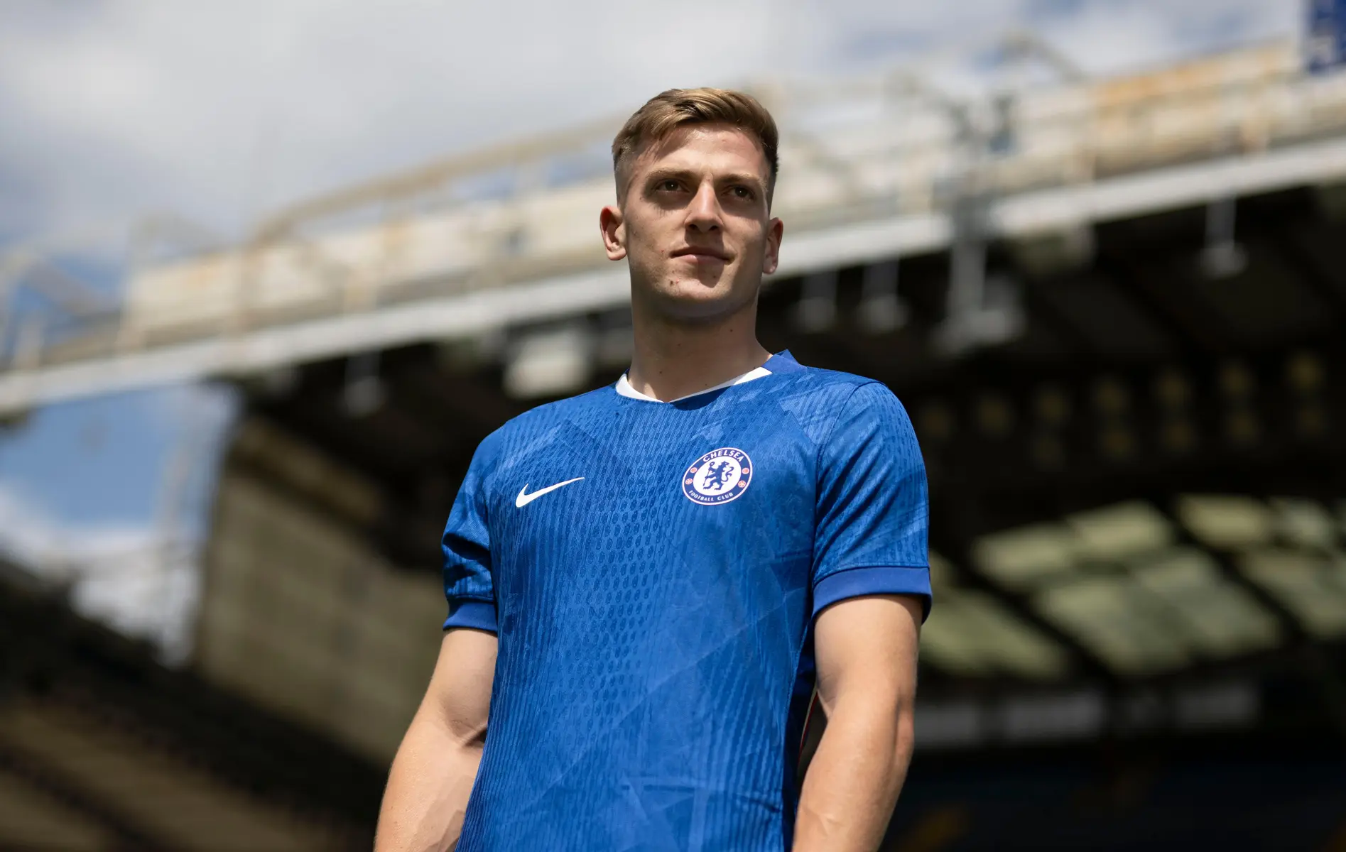 Marc Guiu wearing a blue Chelsea FC home kit standing in a stadium.
