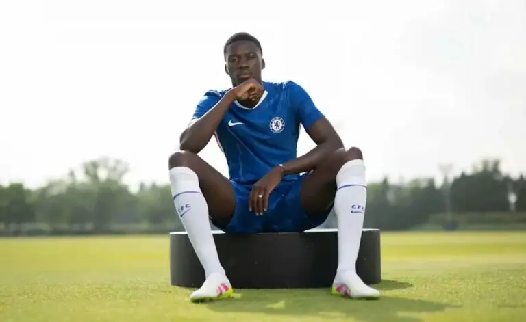 Mamadou Sarr posing in a blue Chelsea FC training kit while sitting on a black circular bench.
