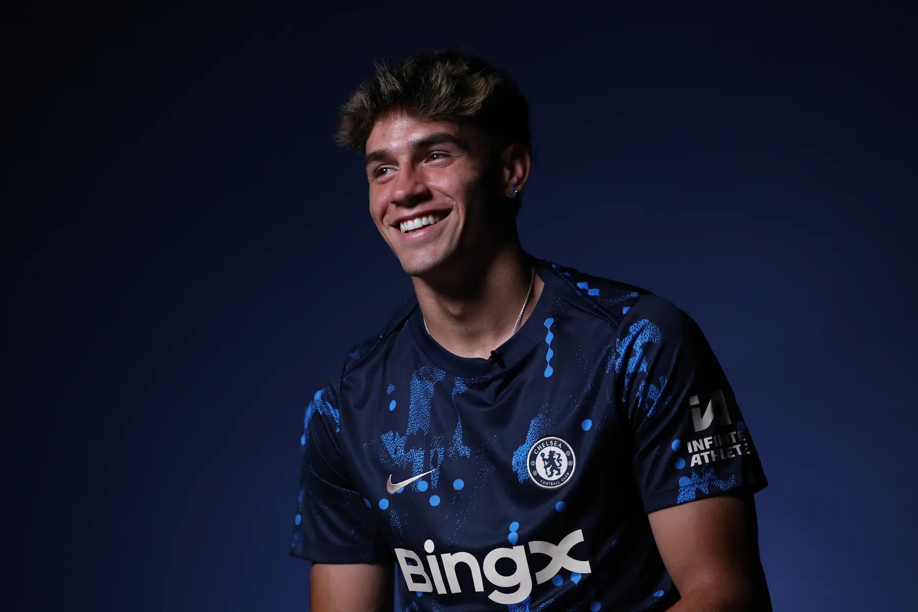 Marc Guiu smiling and wearing a blue Chelsea FC jersey with the BingX sponsor logo