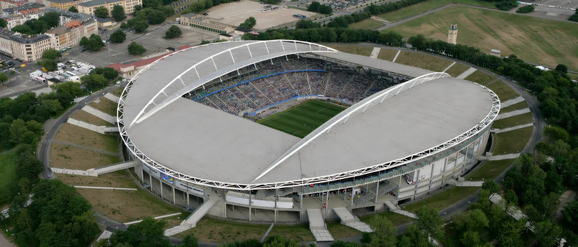 Aerial panoramic view of the Red Bull Arena stadium in Leipzig, featuring its distinct white roof and green pitch.