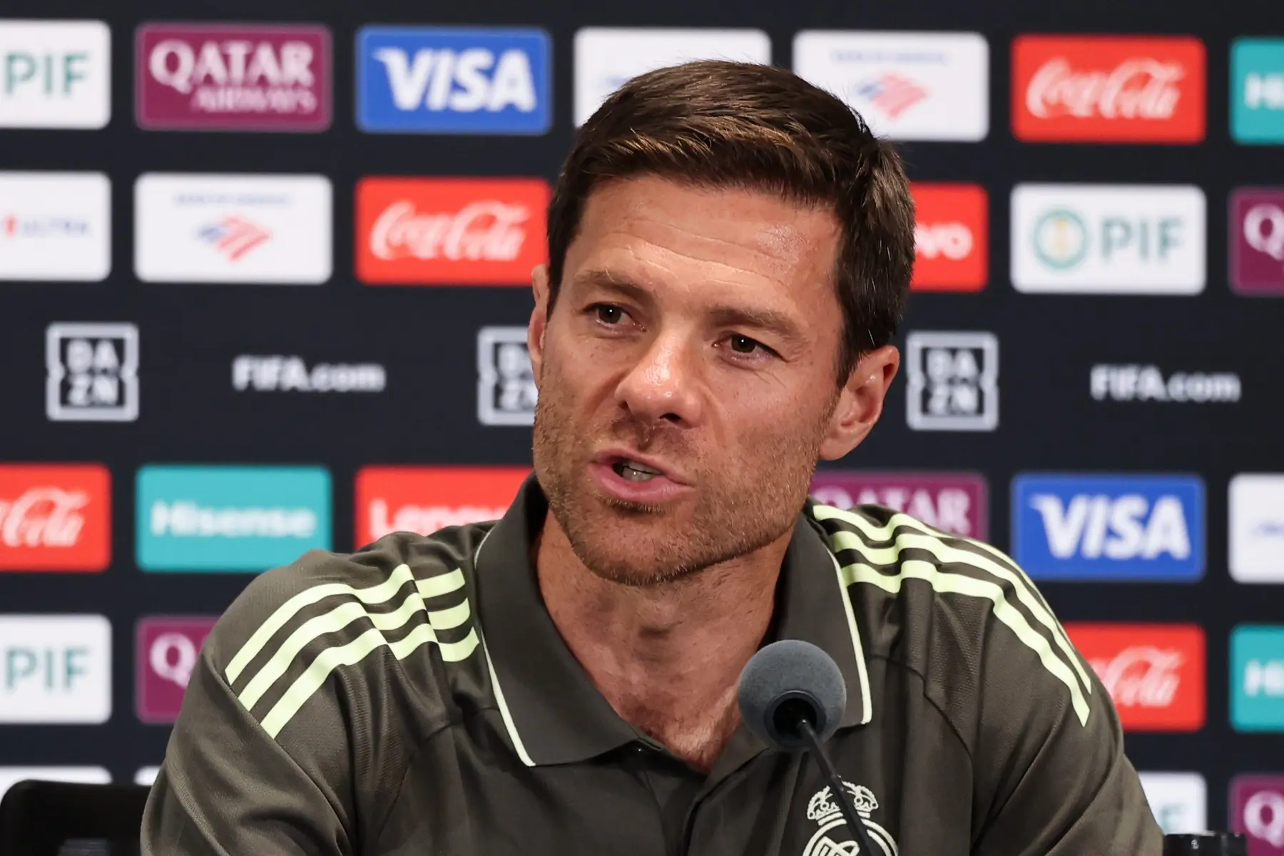 Xabi Alonso speaking at a press conference with sponsorship logos in the background