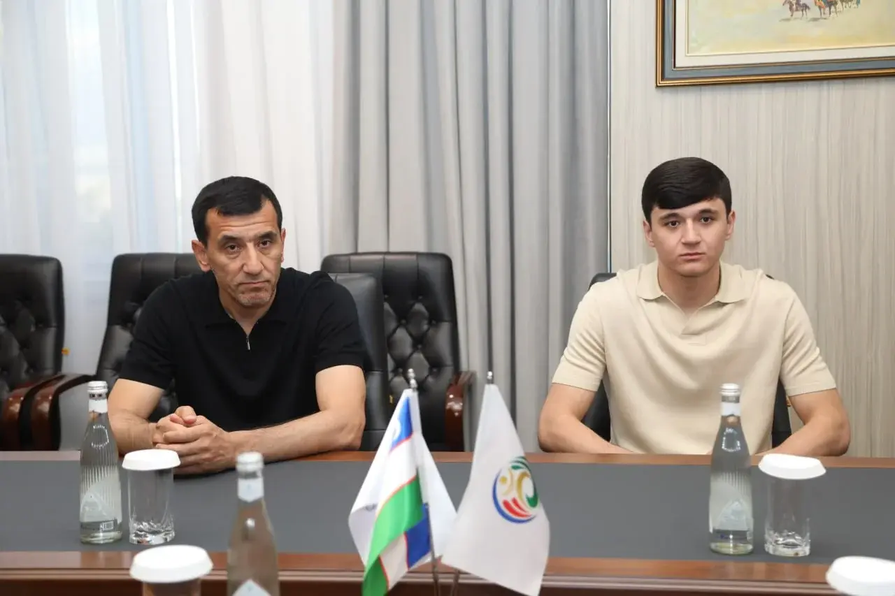 Khikmatjon Khashimov and Abdukodir Khusanov seated at a conference table with flags in front of them.