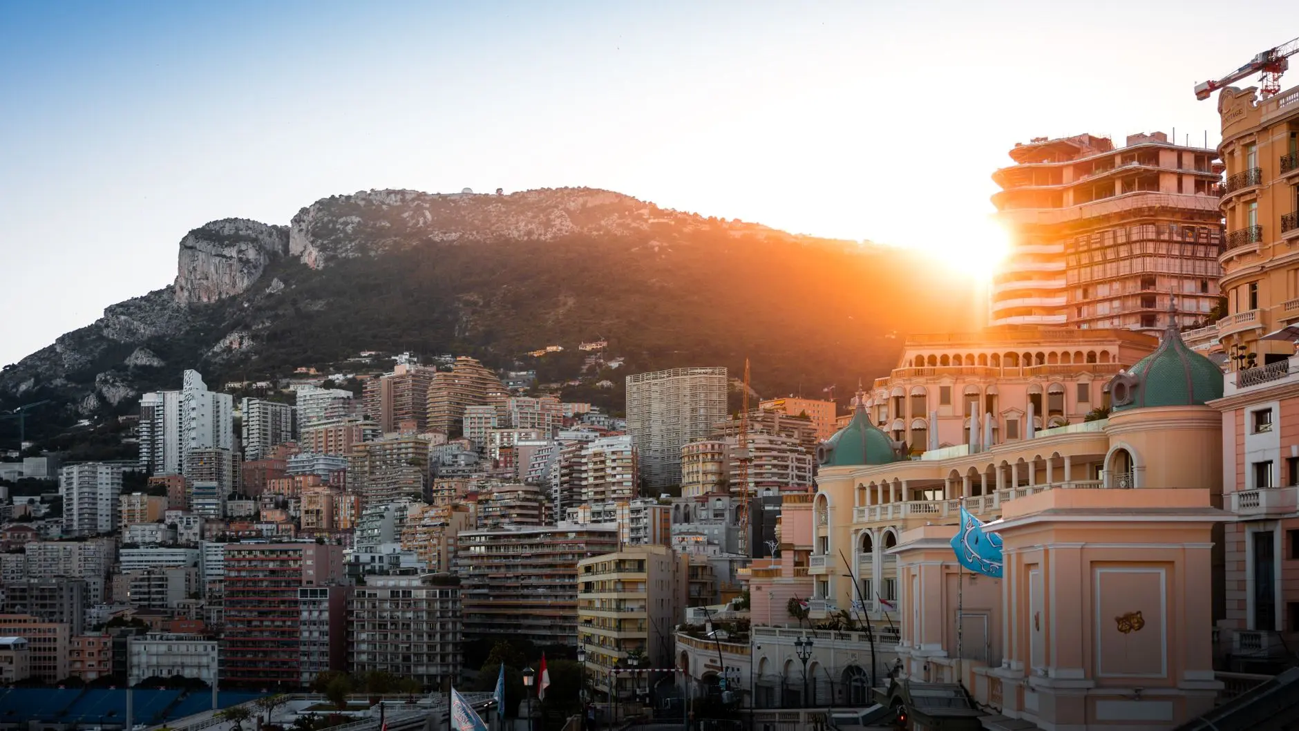Panoramic sunset view of Monaco city buildings with a rocky mountain backdrop