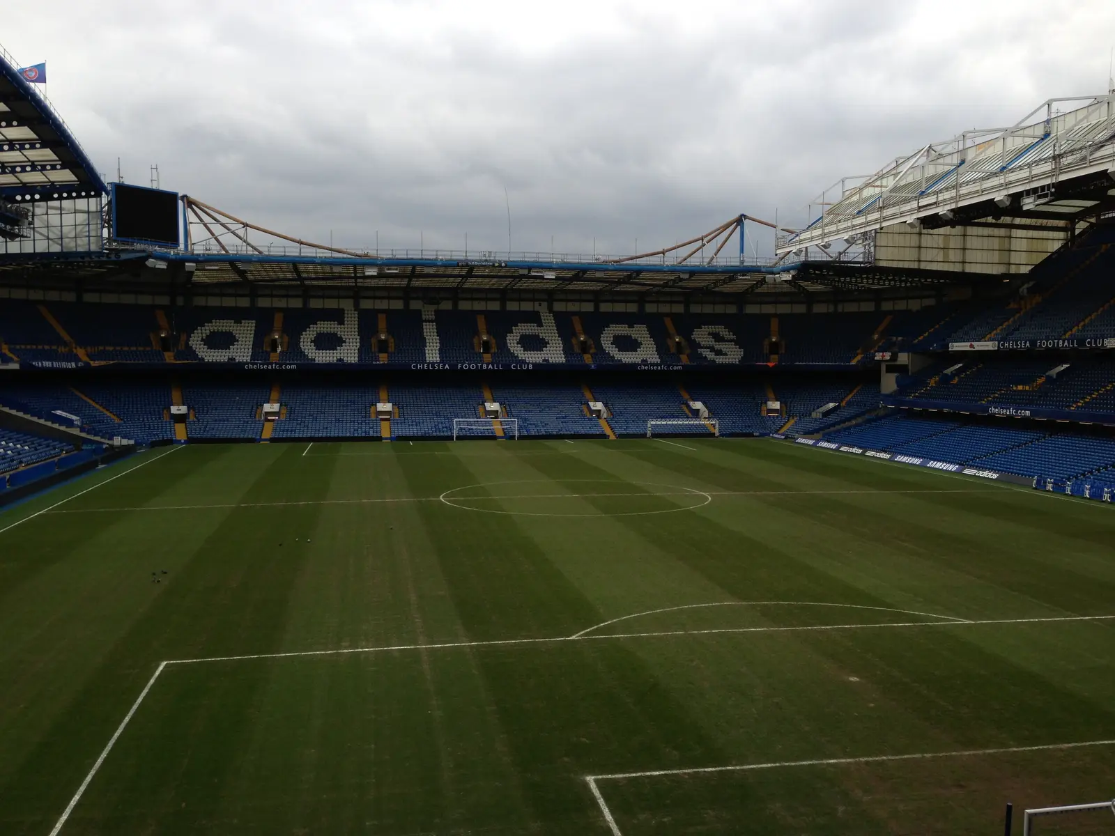 A wide view of the football pitch at Stamford Bridge stadium with blue seating and an Adidas banner.