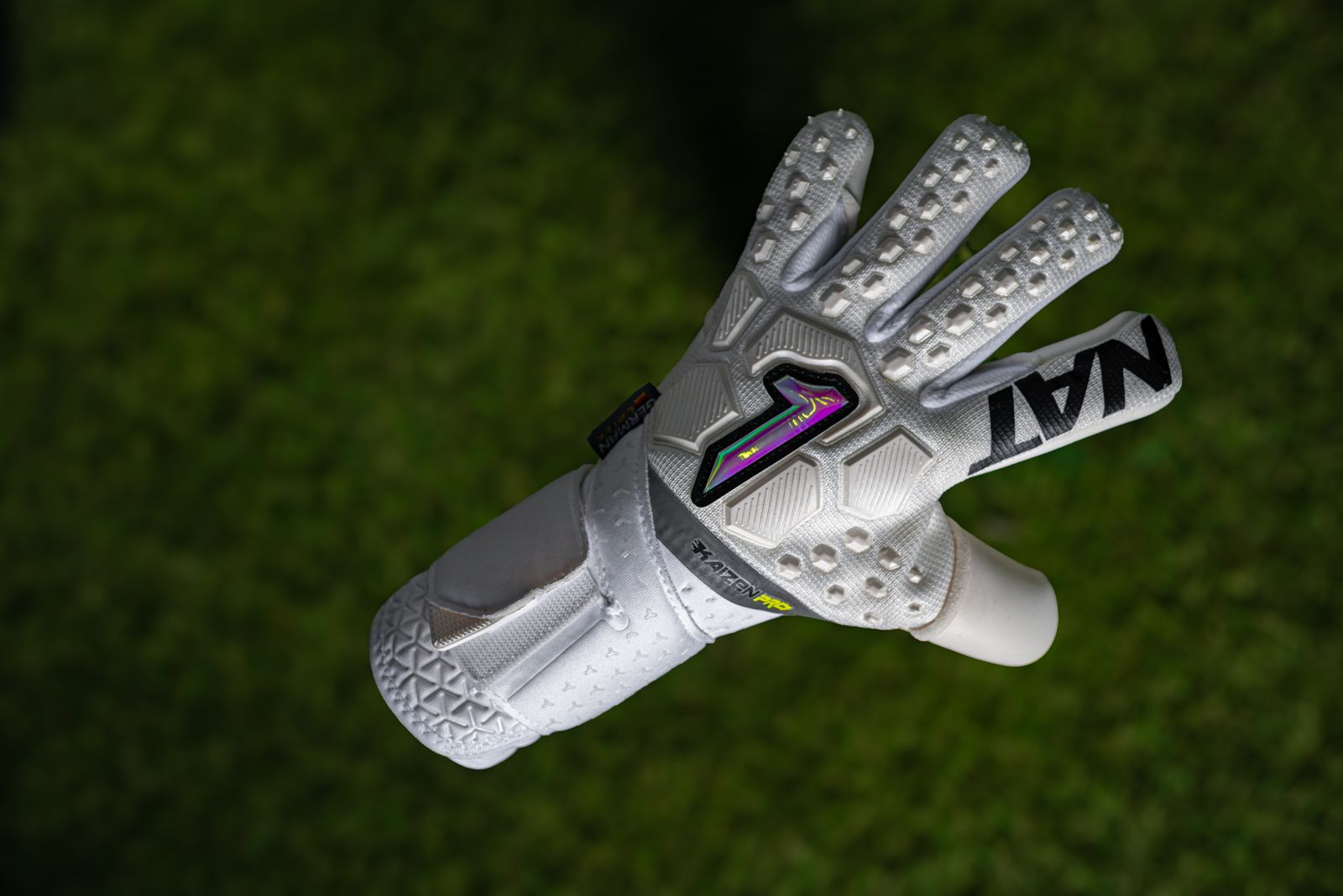 White goalkeeper glove held up against a blurred green football pitch