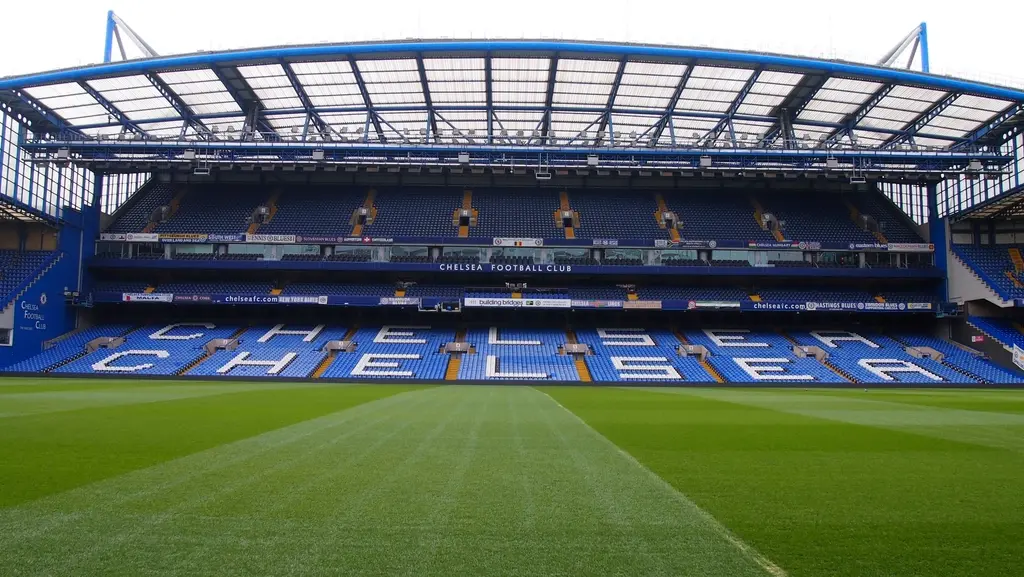 A wide view of the empty stands and pitch at Stamford Bridge stadium, with Chelsea Football Club branding visible.